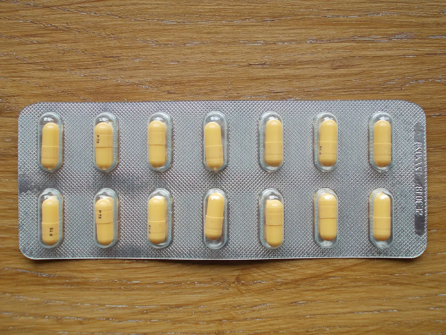 The front of a blister strip of yellow capsules on a wooden table