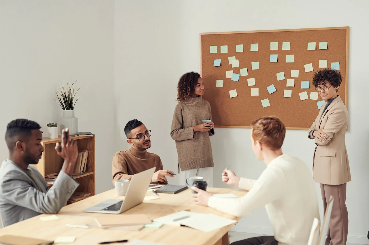 Five people in a meeting room around a table with a laptop and coffee cups